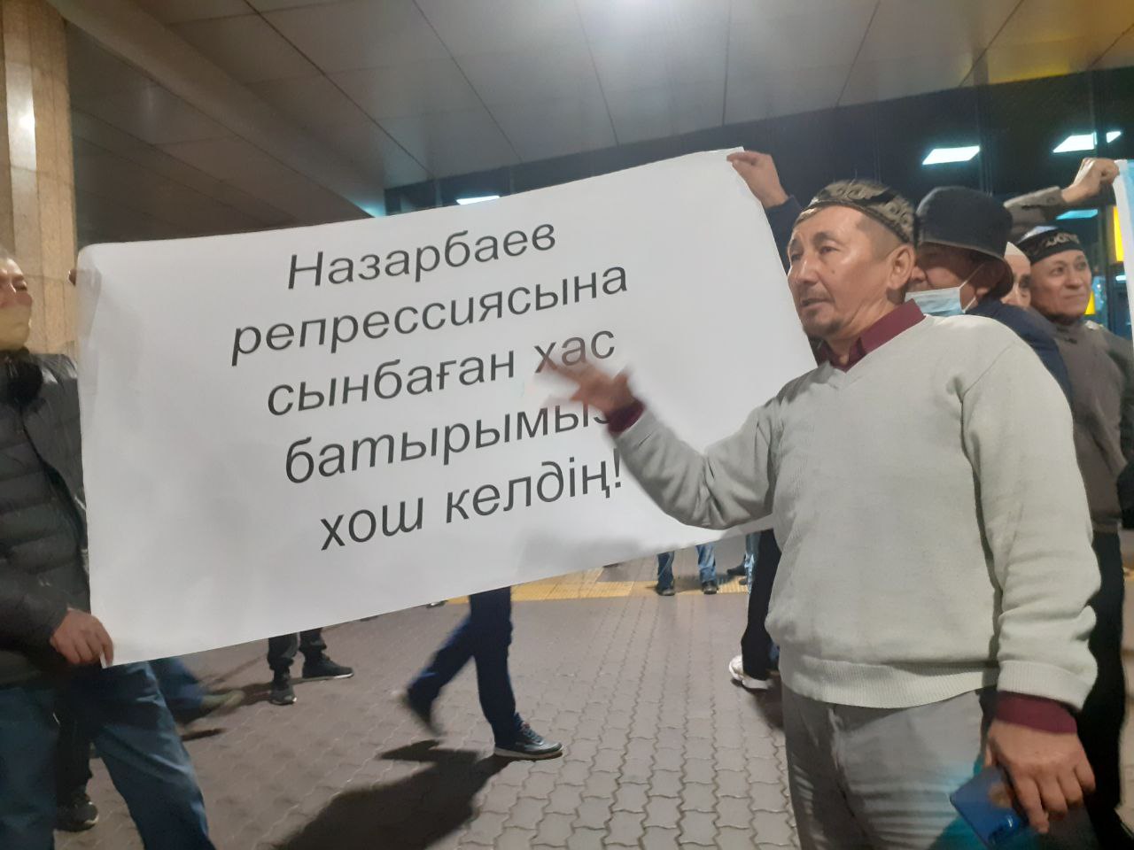 Белсенділердің бірі «Назарбаев режиміне сынбаған хас батырымыз, қош келдің» деген жазуы бар плакаттың қасында азаматтық-жеке көзқарасын білдіріп тұр. Фото: QT